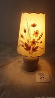 Lit lamp showing warm glow through pressed flower floral shade on a pottery base.