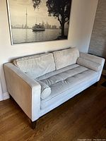 Light grey plush couch against a wall with a black and white cityscape image above it, featuring two back cushions and two bolster pillows on wooden legs.