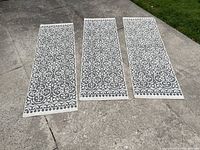 Three identical rug runners laid on a concrete surface showing black and white scroll pattern.
