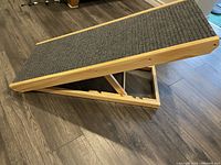 Top angled view showing textured dark gray carpet ramp surface on light wooden frame with side rails.