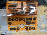Orange plastic case open showing assortment of taps, dies, and handles neatly arranged inside.