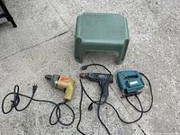 Full lot image showing two drills, one electric jigsaw, and a small green step stool placed on concrete ground.