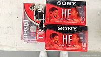 Unopened Sony HF 60 minute and Maxwell UR 90 minute cassette tapes shown in original packaging and cases.