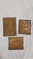 Three copper trench art panels arranged on a light fabric background, showing all items in the lot
