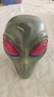 Front view of green alien head sculpture showing large red eyes and smooth surface.