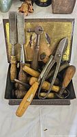 Top view of tin containing antique chisels, punch tool, snips, and wooden handled tools.