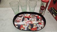 Lot items arranged on a surface with three Coca-Cola glasses, Santa-themed tray, and Coca-Cola metal tin visible