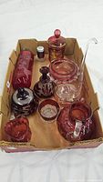 Photo showing various cranberry glass items including vases, jars, bowls, and pitchers with etched and gold floral details.