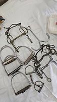 Overview of all horse saddle parts including foot stirrups and various bits on white cloth background
