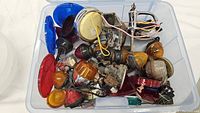 Top view of a container filled with diverse vintage car lights with red, amber, blue, and clear lenses, some with wiring attached, and various car parts.