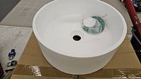 Top view of new white round basin sink showing interior and drain hole with included drain stopper wrapped in plastic.