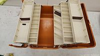 Top view of the opened fishing tackle box showing multiple beige plastic trays for organizing tackle and gear.