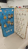 Front left and right panels of display showing multiple vintage padlocks and numerous key hooks, with original labels on blue and white panels.