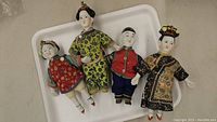 Four vintage 1930s Asian porcelain dolls lying on white tray, showing full body views with traditional clothing.