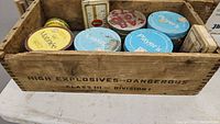 Wooden box showing label 'High Explosives-Dangerous Class III Division 1', containing various vintage tobacco tins including Player's and others