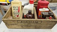 Wooden crate with various vintage oil and polish containers including Wolf's Head Outboard Motor Oil can.