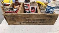 Wooden box filled with assorted vintage automotive supply products, showing branding and product labels.