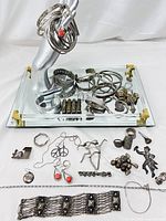 Wide view of assorted scrap silver jewelry on mirrored surface with display hand showing bangles and rings, including various bracelets, necklaces, rings, and pendants.