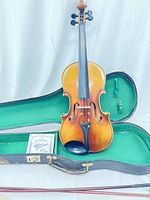 Front view of one vintage violin standing inside open green lining case with some accessories visible