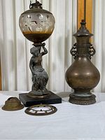 Both lamps side by side on a white surface showing overall size comparison and condition, including missing lamp parts and metal statue base details.