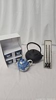 Full view of all items in the lot including cast iron tea pot, ceramic tea pot, boxed tea cups set, and boxed tea stirrers.