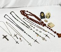 Photo showing multiple rosaries and religious pendants laid out on white fabric.