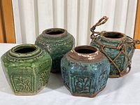 Overview of four ginger jars with two green and two blue jars placed on white tablecloth, showing variations in glaze and one blue jar with rattan holder.