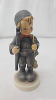 Front view of Goebel Hummel Chimney Sweep porcelain figurine showing the boy holding a brush and wearing a grey suit and cap.