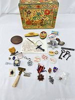 Full view of the assorted vintage jewelry, pins, medals, keys, trinkets, and floral metallic box showing overall items included in the collection.