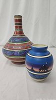 Two pottery items including a tall long-necked jug with colorful geometric patterns and a smaller vase with a blue and purple wolf sunset design.