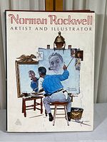 Front cover of the hardcover coffee table book 'Norman Rockwell Artist and Illustrator' showing an image of Rockwell painting a self-portrait.