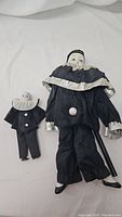 Two vintage handcrafted porcelain dolls, one clown and one mime, laid flat showing full outfit and face details
