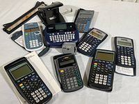 Overview photo showing 7 calculators with slip-on covers, Brother P-touch label printer, two paper hole punchers, and ruler.