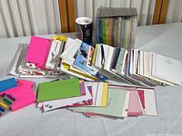 Photo showing a large collection of unused greeting cards spread out on a table with various colors and patterns. Also visible is a box of assorted colored envelopes and a sealed box of a desktop puzzle.