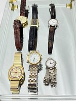 Top view of six assorted vintage wristwatches laid out on a reflective surface, showing dial faces and bands