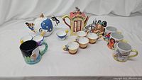 Wide view of full lot showing all teapots, teacups and mugs arranged on a white fabric background