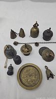 Lot of various vintage Indian brass bells and a round engraved brass plate displayed on white background.