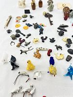 Overview of varied miniature collectibles including glass animal figurines, metal keys and thimble, vintage pins, and ceramic animals on a white background.