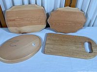 Photo showing three wooden plaques (two rectangular with decorative edges and one oval with hanging hook) alongside a small rectangular wooden cutting board with handle cut-out, all on a table surface.
