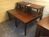 Pair of mid century end tables stacked showing wood legs and laminate tops.
