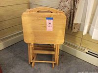 Front view of four wooden folding TV trays stacked together with visible handle and condition sticker.