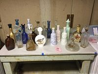 Full lot of vintage liquor bottles displayed on table showing variety of colors, shapes, and designs.