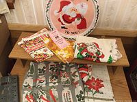 Full lot showing folded Christmas linens arranged on a shelf, including napkins, Santa print tea towels, and round tray with Santa motif.