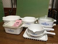 Photo showing multiple CorningWare Cornflower Blue dishes including rectangular and round casseroles, divided saucepans, glass lids and white tray.