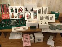 Overall view of multiple boxed Dept 56 Snow Village accessories including figurines and light sets on table.
