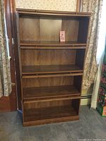Front view of barrister bookcase without doors, showing four shelves with wood grain finish and brass rails along the front.