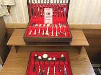 Full view of the open dark wood storage chest presenting the flatware set for twelve with red felt lining and slots for each piece.