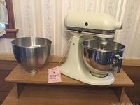 Ivory KitchenAid K45 mixer with one stainless steel mixing bowl attached and one additional bowl beside it on a wooden surface. KitchenAid food grinder attachment in front of bowls.