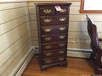 Full front view of the lingerie chest showing seven drawers with brass handles adjacent to wood-paneled wall.