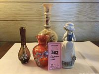Photo showing Lladro figurine with four floral vases arranged on a wooden surface with a MaxSold lot tag visible.
